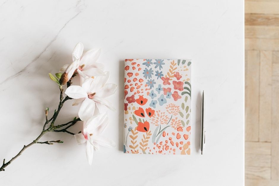 A floral reading notebook with a pen and a small branch of flowers.