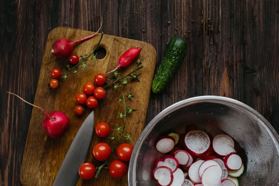 Fresh market vegetables arranged beside a bowl on a wooden table.